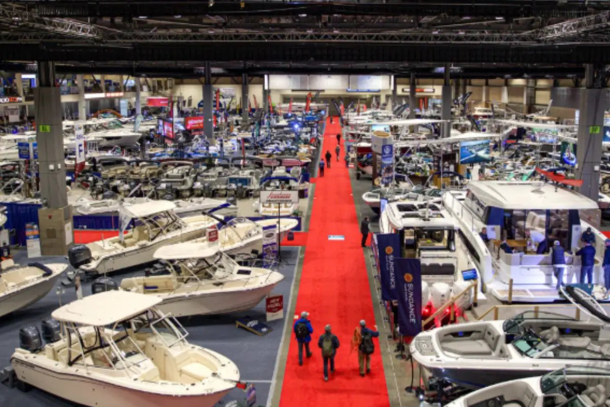 Main exhibition floor at the Seattle Boat Show inside Lumen Field Event Center. Rows of fishing boats and cruisers with a red carpet aisle. Visit Booth North 141 to see Rover Marine and POP Board Co.
