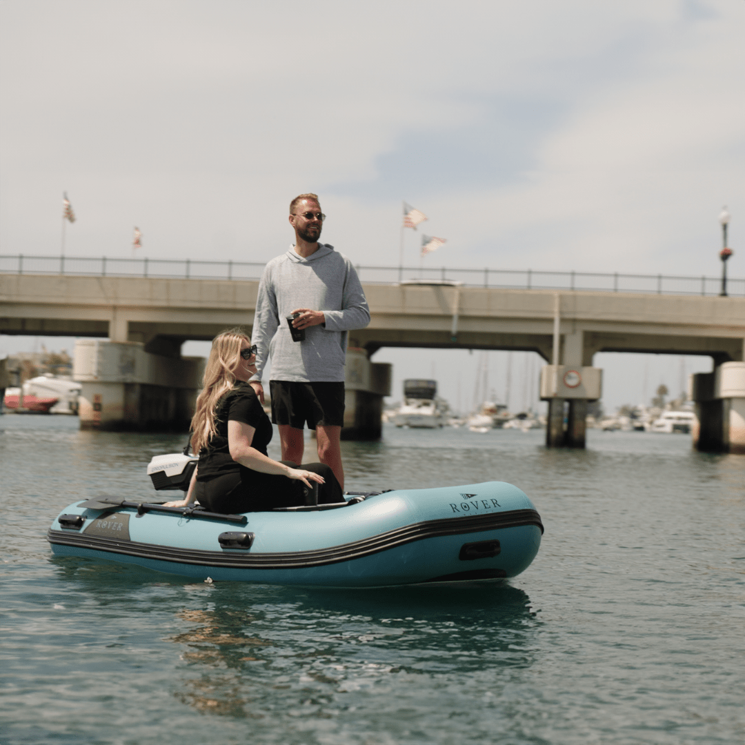 Couple on a Rover Marine inflatable boat with electric motor cruising near a marina bridge.