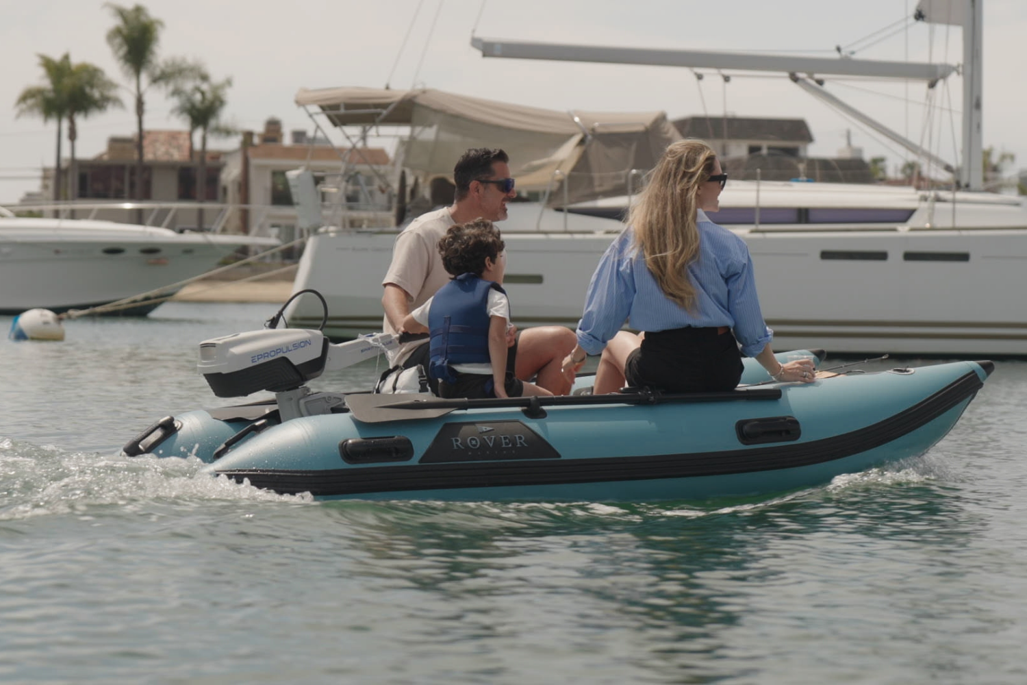 Family riding a Rover Marine inflatable boat with Epropulsion electric motor near sailboats at the marina.