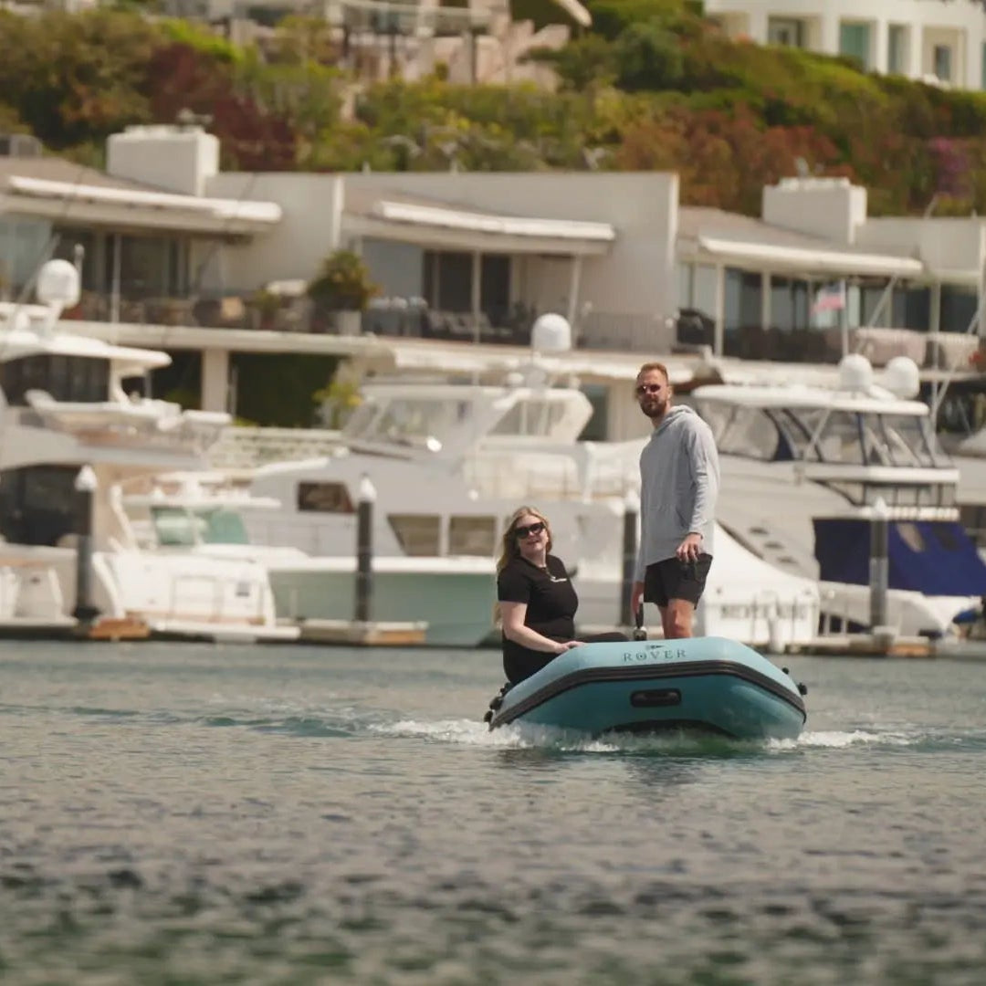 Couple riding a Rover Marine inflatable dinghy in a harbor with yachts in the background
